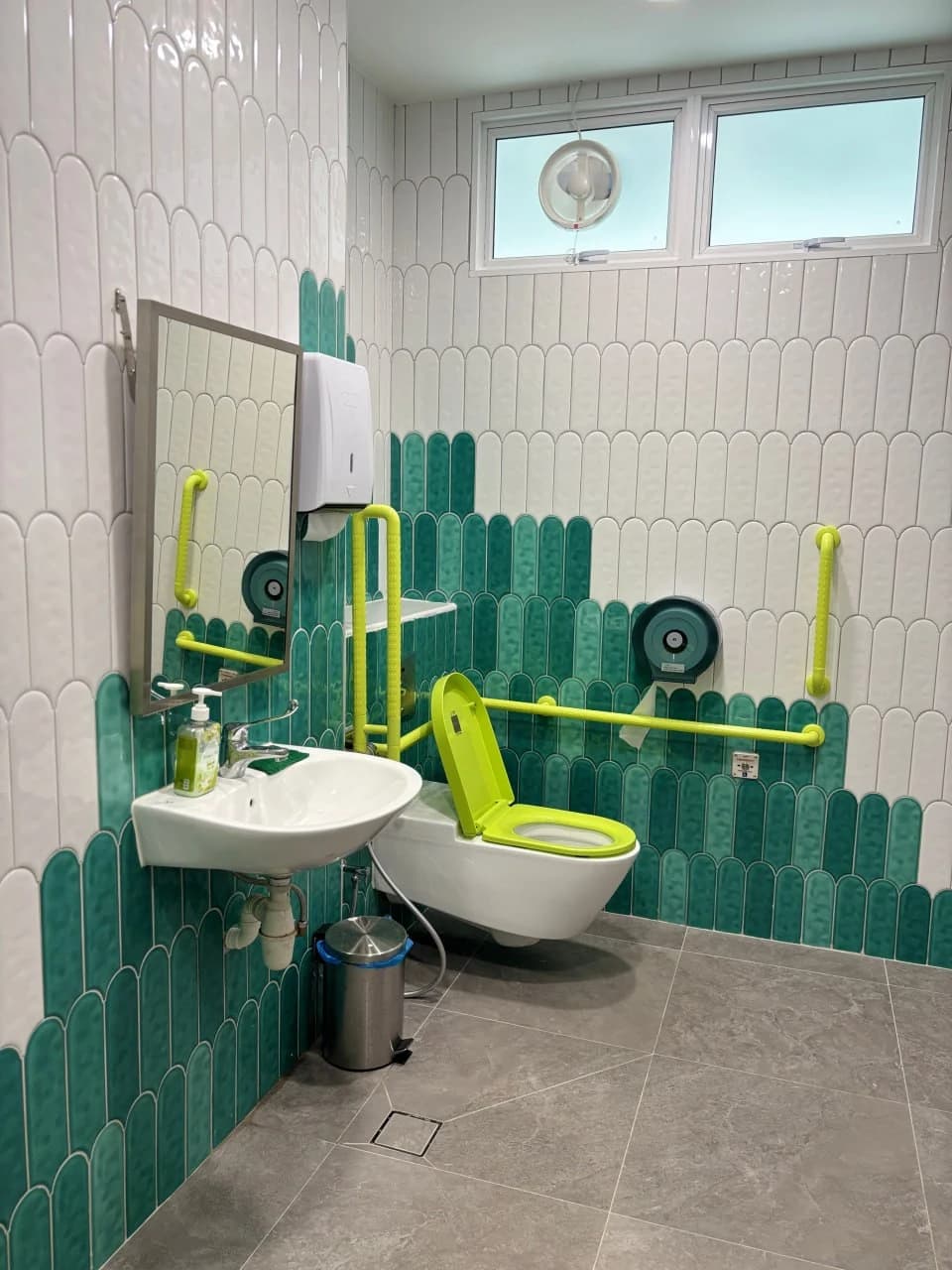 Accessible washroom with teal scalloped tiles and high-contrast support rails at NTUC Health Marsiling