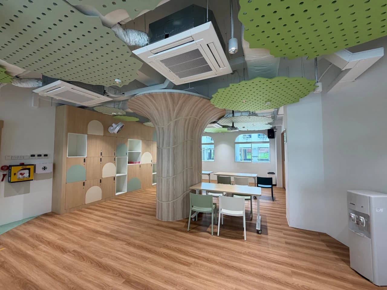 NTUC Health Marsiling community activity space with a sculptural timber column and layered green acoustic ceiling panels